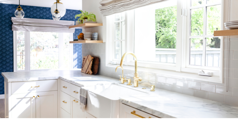 Bright kitchen with large windows, white cabinetry, and light finishes showing how to make your house brighter with natural sunlight.